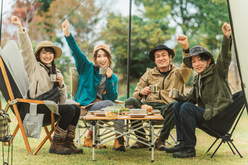 秋冬のキャンプ場で仲間と一緒にコーヒーを飲むアジア人男女
