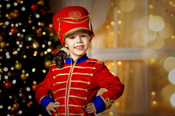 A boy in a nutcracker costume plays with the mouse symbol of the year. christmas tree and gifts