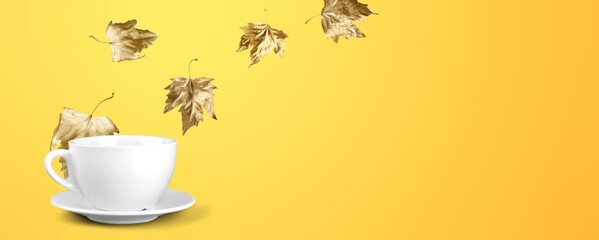 Autumn leaves with ceramic cup on color background.