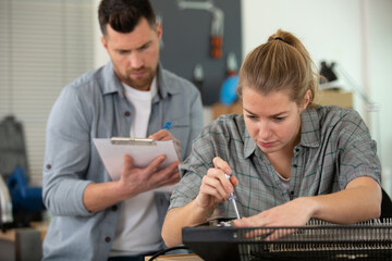 woman repairing a heater colleague behind writing on clipboard