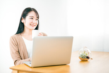 家でノートパソコンを使って映画や動画・ネットショッピングを楽しむアジア人女性
