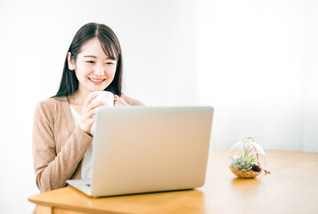 家でノートパソコンを使ってテレワークやネットショッピングする日本人女性
