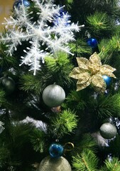 Christmas decorations on the branches of a spruce - a fluffy snowflake, a golden flower, blue and grey balls