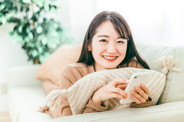 ソファでスマホを使う笑顔の日本人女性
