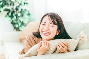 家のソファに寝転びながらリラックスして爆笑する笑顔の日本人女性
