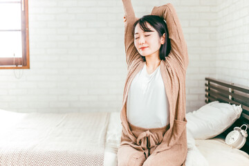 朝ベッドルームで起床するパジャマ姿の日本人女性
