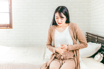 ベッドルームで腹痛・生理痛に苦しむ日本人女性
