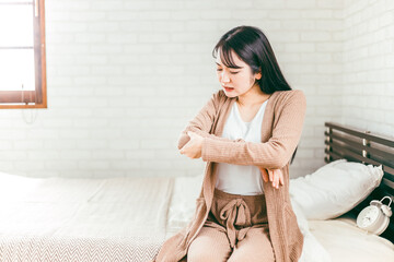 ベッドで肘を触りリウマチ・関節痛に悩む日本人女性
