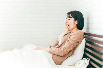 ベッドルームで眠くてあくびをする日本人女性
