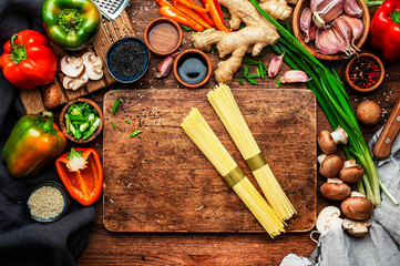 Fototapeta na wymiar Food background. Asian cuisine cooking ingredients. Paprika, mushrooms, ginger, lime, garlic, soy sauce and egg noodles on wooden kitchen table. Healthy eating concept. Top view