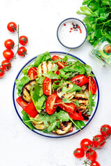 Healthy vegan salad with grilled vegetables, paprika, zucchini, eggplant with fresh tomatoes and mixed herbs. White table background, top view