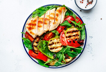 Healthy salad with grilled chicken breast fillet and vegetables: paprika, zucchini, eggplant, fresh tomatoes and mixed herbs. White table background, top view