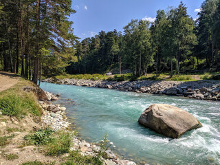 Arkhyz, Karachay-Cherkessia, Russia - August 26, 2022: View of the Zelenchuk River in the village of Arkhyz against the backdrop of a coniferous forest. Large stone lies in the middle of the river