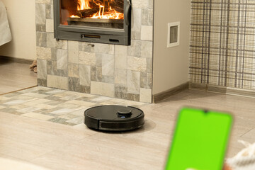 Smartphone screen with chromakey against cozy light room. Modern black robotic vacuum cleaner...