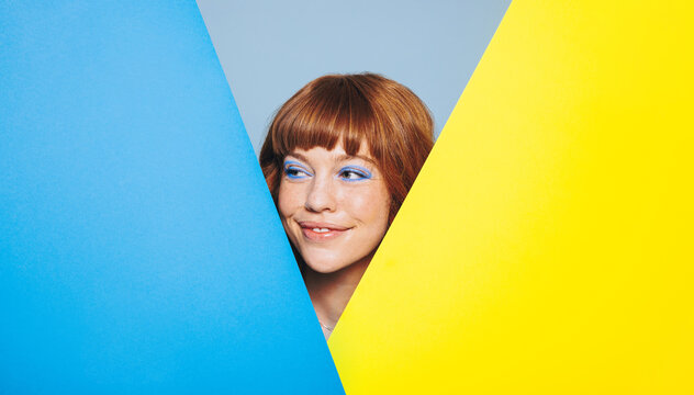 Fototapeta Happy woman with ginger hair and blue eye shadow standing behind colour placards