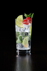 A highly carbonated ice drink with raspberries, lime wedges and mint on a black background. Selective focus.