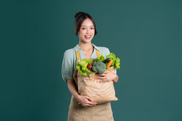 Asian girl portrait holding a bag of vegetables on a green background