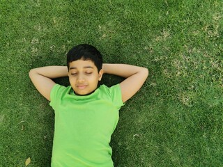 Child boy lie down on grasses or lawn under warm sunlight. Kid  closed his eyes and flew...