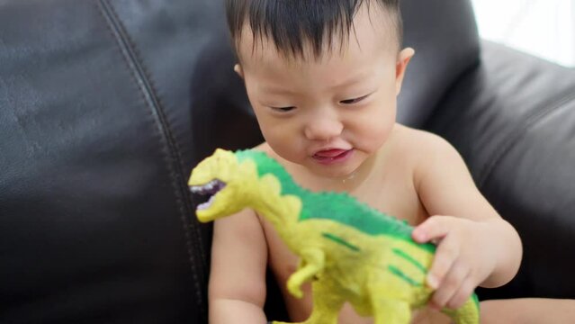 A drooling kid hold the Tyrannosaurus rex toy at sofa