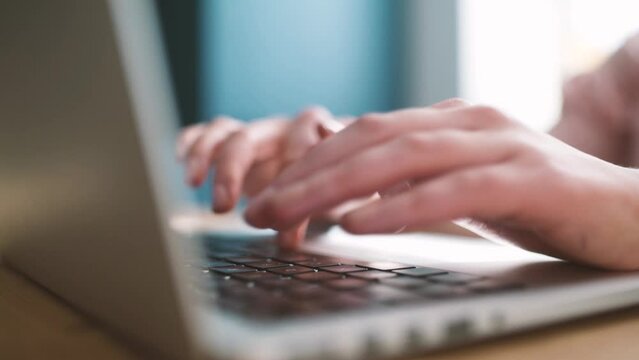 Young professional is working with laptop computer in co-working space. He or she is creating an amazing and innovative online project. You can see fingers slow motion typing on keyboard.