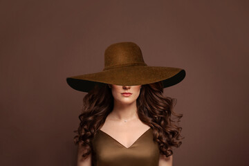 Beautiful curly hair model in wide brown broad brim hat. Woman with wavy long hairstyle and hat portrait.