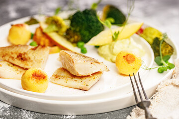 Close-up Baked sea fish fillet with vegetables. Tilapia fillet with broccoli, cherry tomatoes, fried potatoes, green peas and lettuce. Sea food on a white plate. Mediterranean Diet. Selective focus