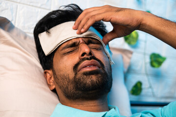 close up head shot of young indian sick man suffering from fever while sleeping at night by placing...