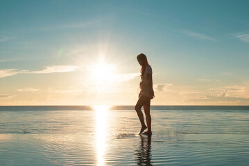 Fototapeta na wymiar Asia woman walking alone the sea view infinity pool in sunrise, morning time