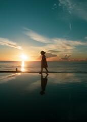 Fototapeta premium A girl walking along the infinity pool sea view in the sunset time.