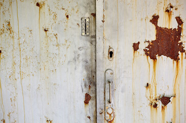 The old door to the building. Painted metal door with rust spots and scratches, entrance to the territory in bad condition