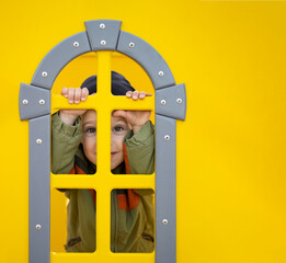 portrait of a boy looking out the window on the playground on a yellow wall with space for text