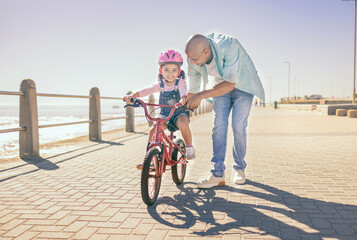Father, child and bicycle with a girl learning to ride a bike on promenade by sea for fun, bonding...
