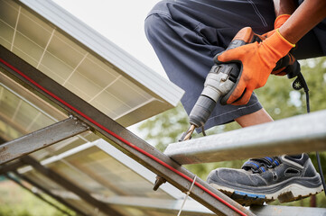 Worker fixing metal beams with electric drill for solar panels. Concept of renewable and ecological energy. Modern technology and innovation. Idea of environment safe. Cropped image of man in workwear