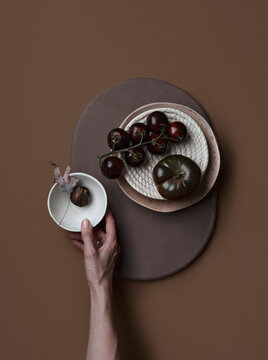 View from above hand reaching for bowl next to dark cherry tomato and black krim tomato
