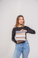 Attractive brown-haired girl in a black top and blue jeans holds a stack of books. Student with books preparing for the exam
