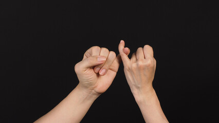 Hands is do a pinky promise gesture on black background