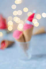 Defocused pink ice cream in Santa hats in a waffle cone on a gray table, background garlands bokeh. Festive frozen dessert