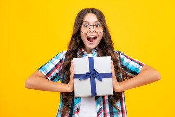 Amazed teen girl. Child with gift present box on isolated studio background. Gifting for kids birthday. Excited expression, cheerful and glad.