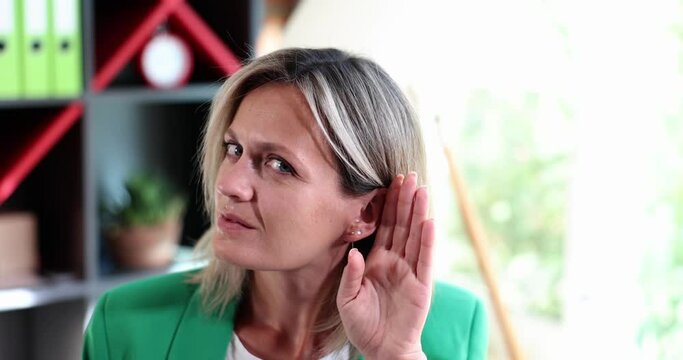 Portrait of curious sly lady eavesdropping with palm of ear in office