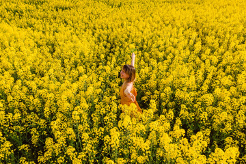 Fototapeta premium Woman in rapeseed field. Yellow flowers and happy woman