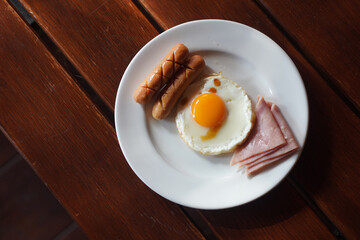 two Sausages, fried eggs, two slices of bacon, in a white dish on a wooden floor background, breakfast, health, decor, fashion, copy space