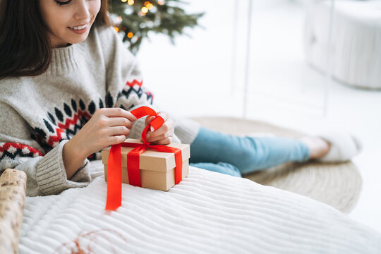 Crop photo of young woman in nordic sweater packing gift box at home