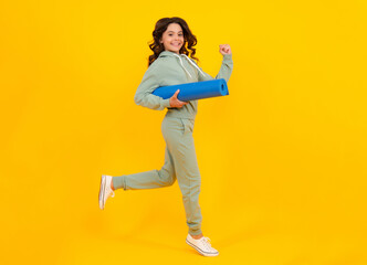 Full length of a fitness teen girl in sportswear hold yoga mat posing over yellow background. Run and jump. Fitness model child wearing sport clothes. Girl in the sport concept.