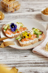 Aesthetic appetizer breakfast with cottage cheese, smoked salmon, arugula, avocado, cucumber and edible flowers. Pescetarian diet.
