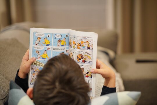 Child reading a Polish Ptys I Bill comic book on a sofa in a living room