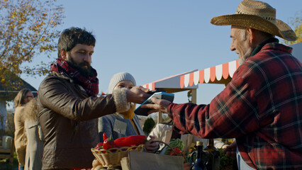 Spouses shopping on local farmers market. Wife stands with basket of fruits or vegetables. Husband...