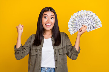 Photo of young japanese khaki shirt woman satisfied excited raise fist up winner jackpot money dollars hooray isolated on yellow color background