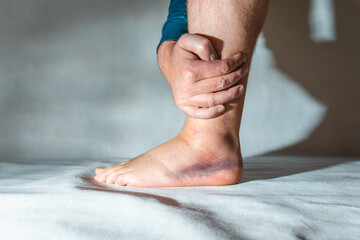 Sprained and swollen ankle.Man hold his sprained ankle at home. Ankle sprain. Injury.White,gray...