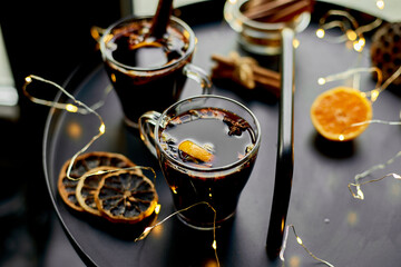 Christmas mulled red wine with spices and oranges on a black table with light garland, traditional hot drink at Christmas, festive cocktail