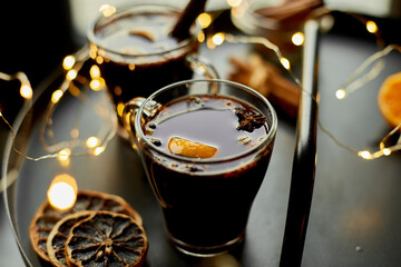 Christmas mulled red wine with spices and oranges on a black table with light garland, traditional...